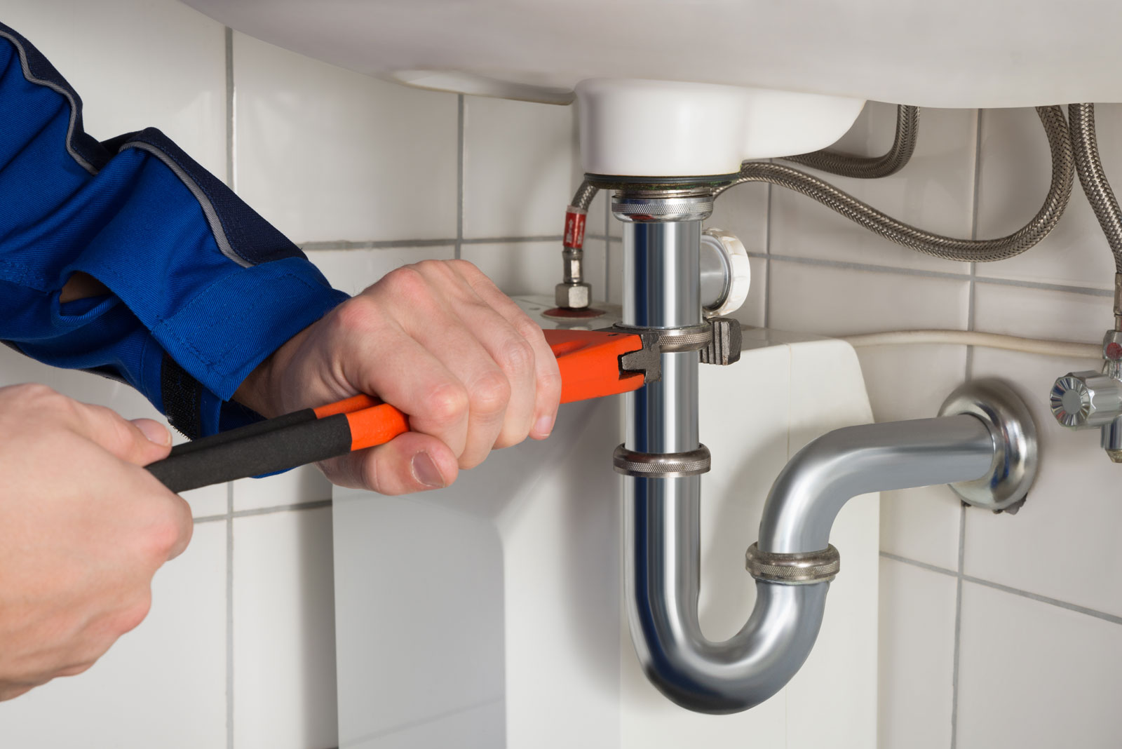 Plumber using a wrench to repair pipes beneath a bathroom sink
